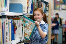 Student selecting a book from a library shelf at school