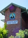 Brick school building with a mounted school crest and the words “Marist College Ashgrove Primary School” visible on the wall, partly framed by surrounding greenery