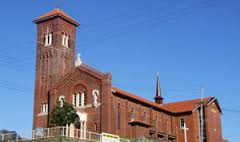 Red brick church building with tall tower and arched windows under a clear blue sky.